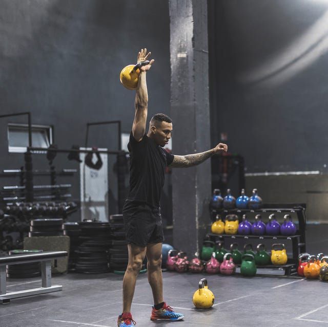 En man utför en enarmad kettlebellpress på ett gym.