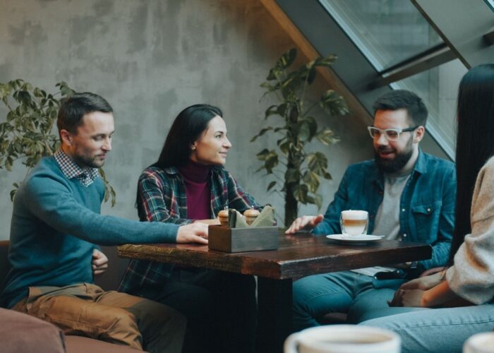 Fyra personer samtalar runt ett cafébord med drycker